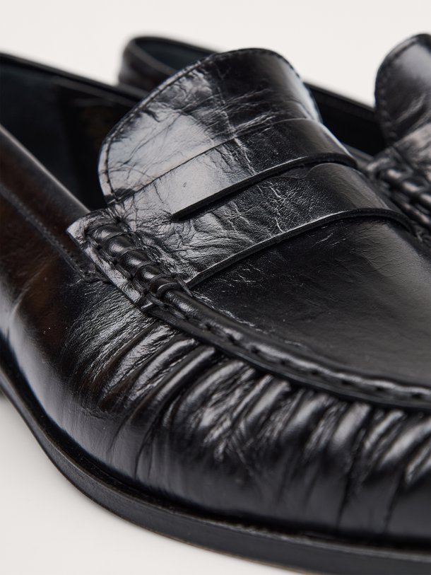 Ontdek de Posa Penny Loafer Wrinkle in zwart leer bij Orangebag. Een tijdloze klassieker met een uniek rimpel-effect voor een moderne, stijlvolle twist.